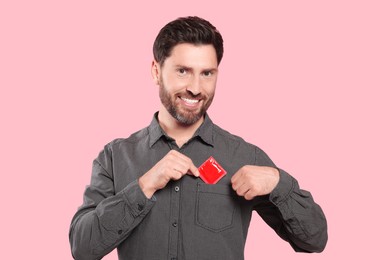 Photo of Man putting condom in his pocket on pink background. Safe sex