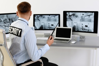 Photo of Male security guard with portable transmitter monitoring home cameras indoors