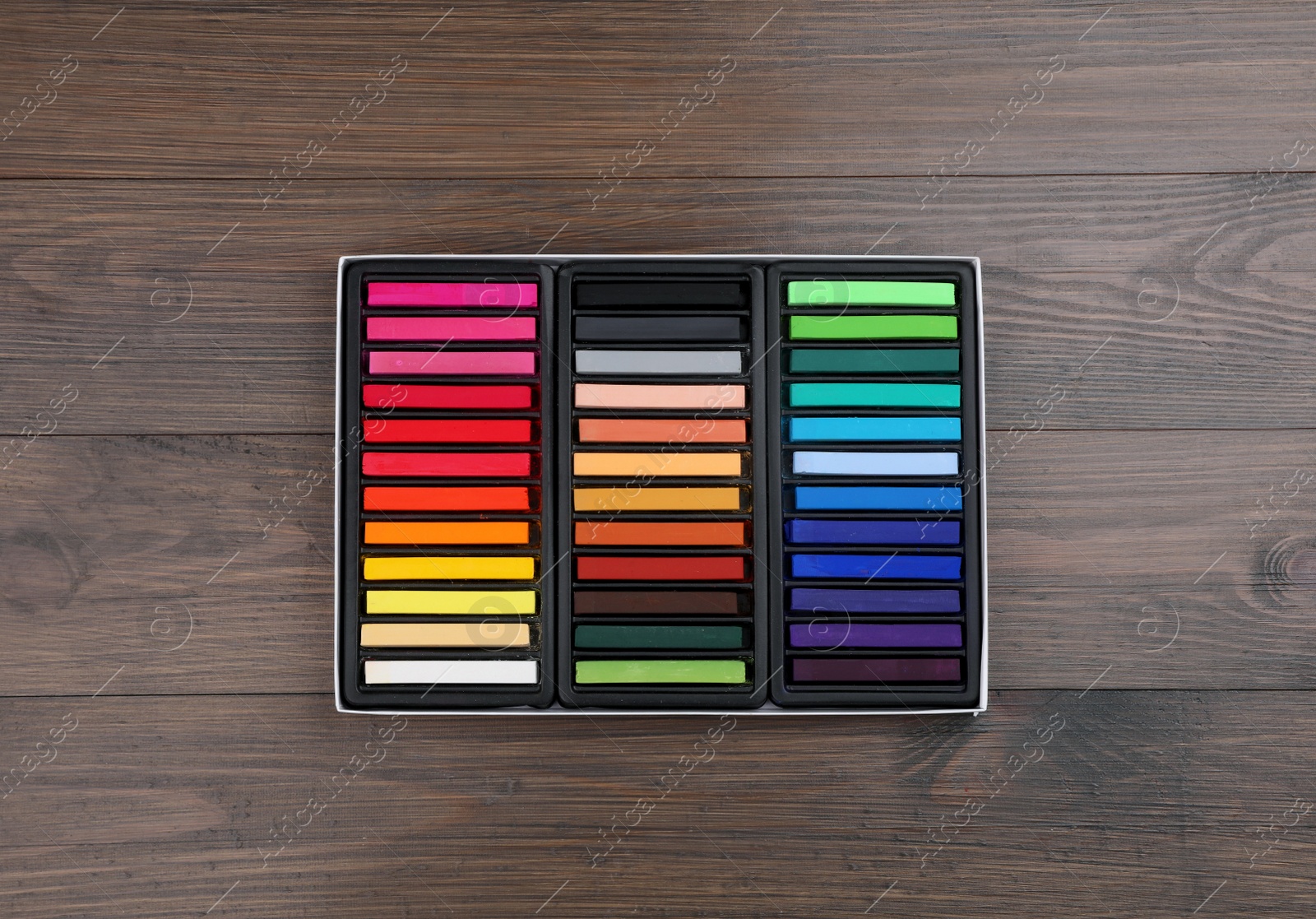 Photo of Set of colorful pastels in box on wooden table, top view. Drawing materials