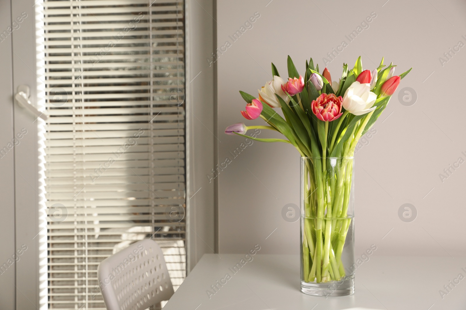 Photo of Beautiful bouquet of colorful tulips in glass vase on table at home