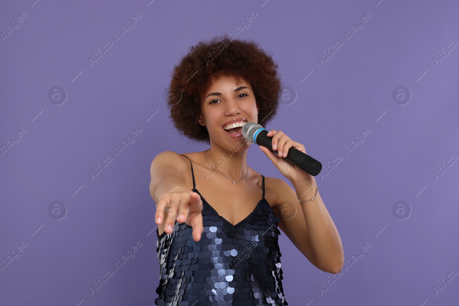 Photo of Curly young woman with microphone singing on purple background