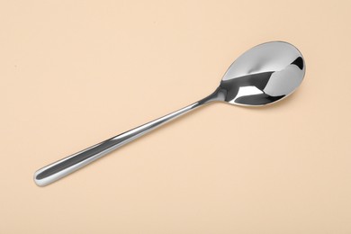 Photo of One shiny silver spoon on beige background, top view