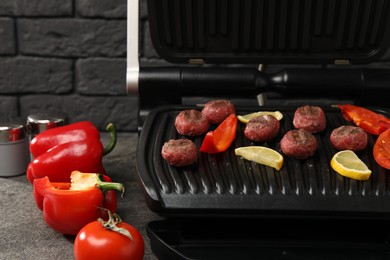 Photo of Electric grill with meat balls, bell peppers and lemon on grey textured table