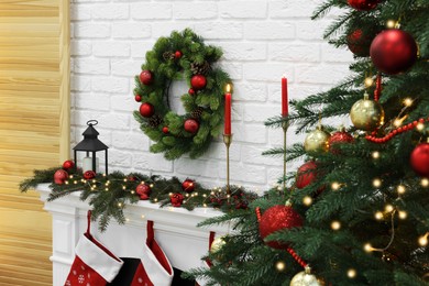 Beautiful Christmas wreath hanging over fireplace near tree indoors