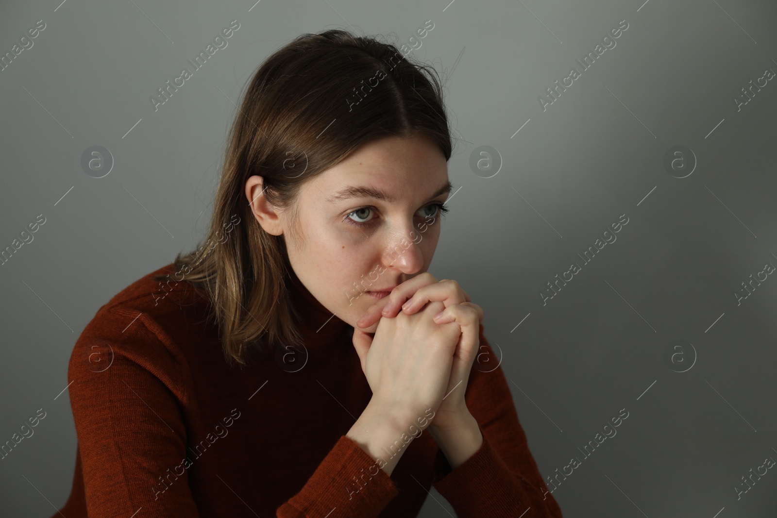 Photo of Sad young woman near grey wall indoors, space for text