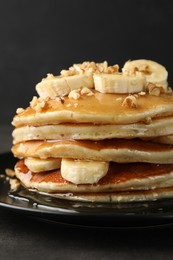 Photo of Delicious pancakes with bananas, walnuts and honey on dark table, closeup