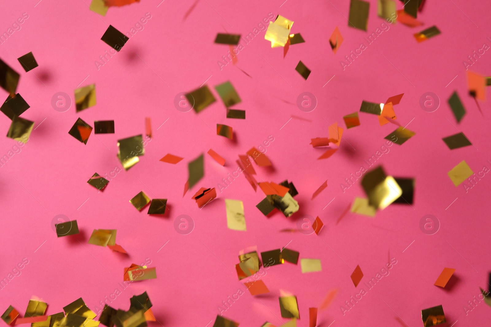 Photo of Shiny golden confetti falling down on pink background