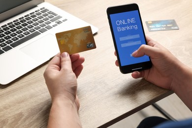 Photo of Man using online banking app on smartphone and credit card at wooden office table, closeup