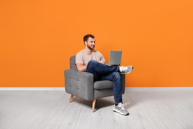 Photo of Young man using laptop while sitting in armchair indoors