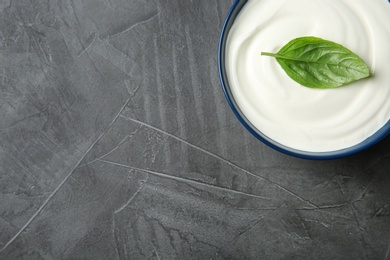 Bowl of fresh sour cream with basil on grey table, top view. Space for text