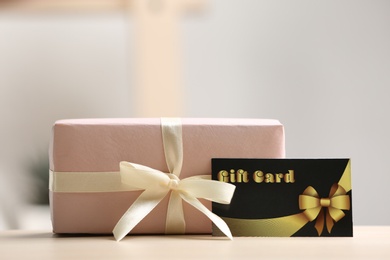 Photo of Gift card and present on table against blurred background, space for text