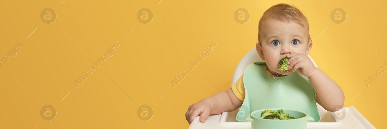 Image of Cute little baby wearing bib while eating on yellow background, space for text. Banner design