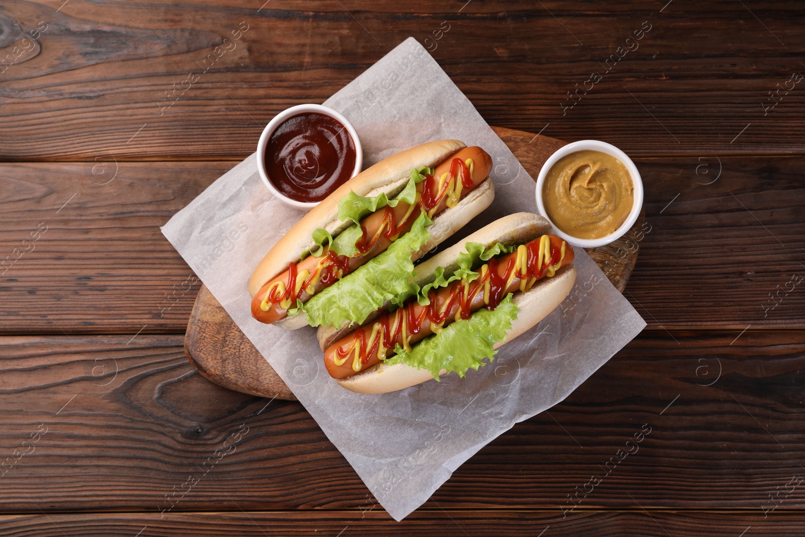 Photo of Tasty hot dogs with lettuce, ketchup and mustard on wooden table, top view