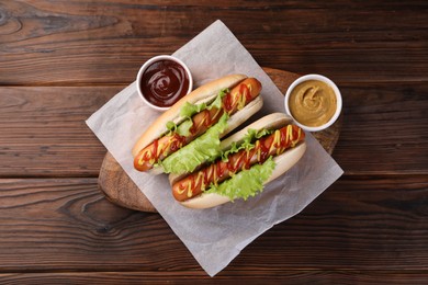 Photo of Tasty hot dogs with lettuce, ketchup and mustard on wooden table, top view