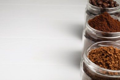Photo of Jars with instant, ground coffee and roasted beans on white table, space for text