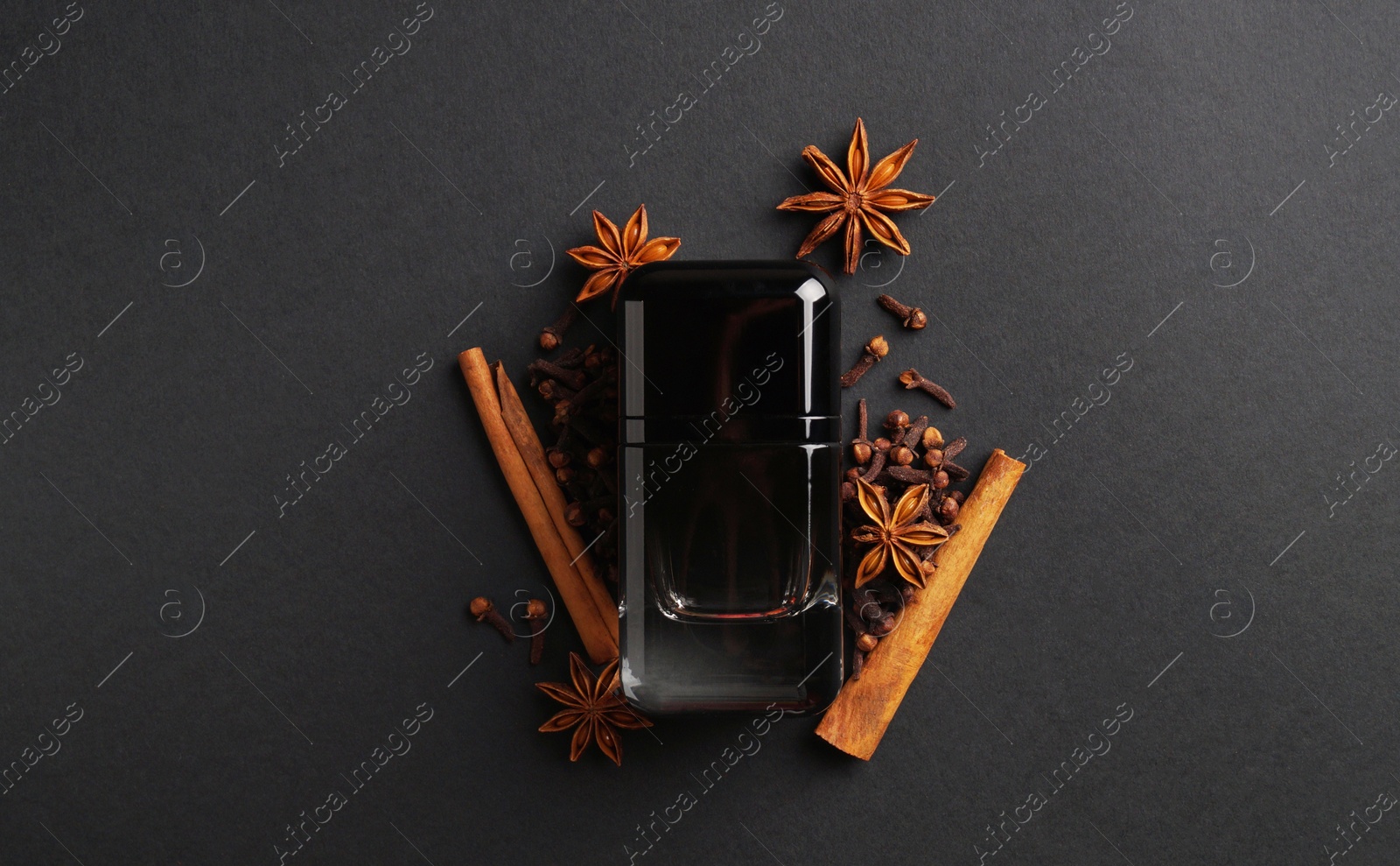 Photo of Bottle of perfume and different spices on dark background, top view