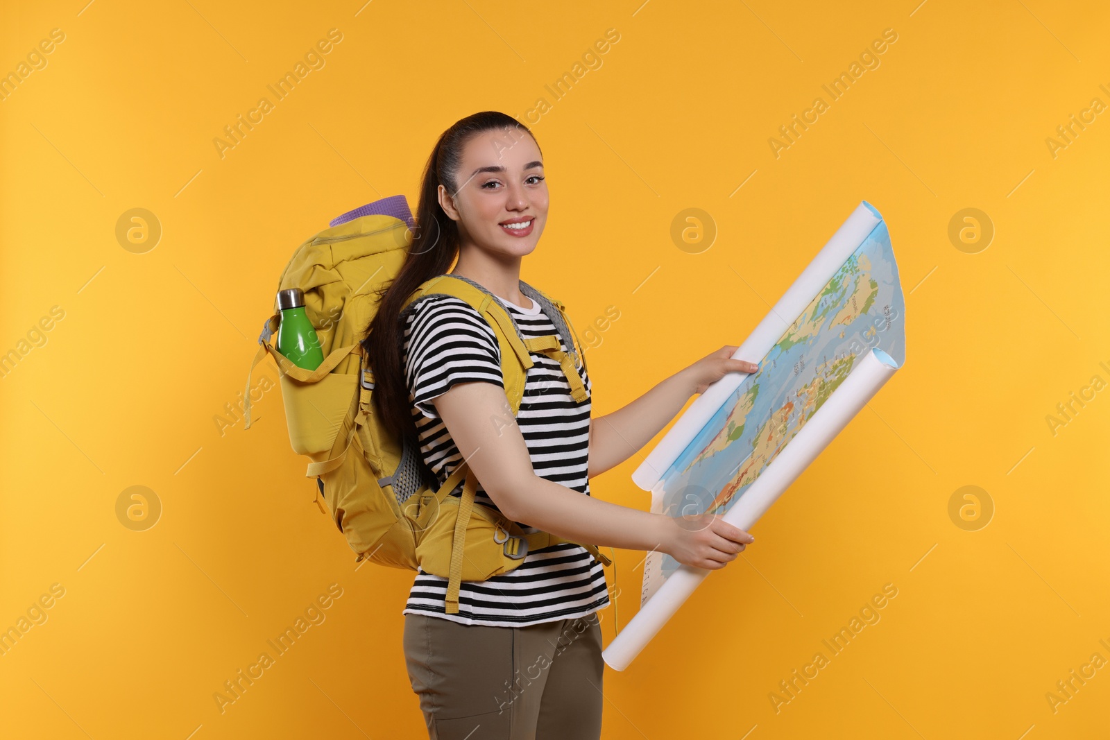 Photo of Smiling young woman with backpack and map on orange background. Active tourism