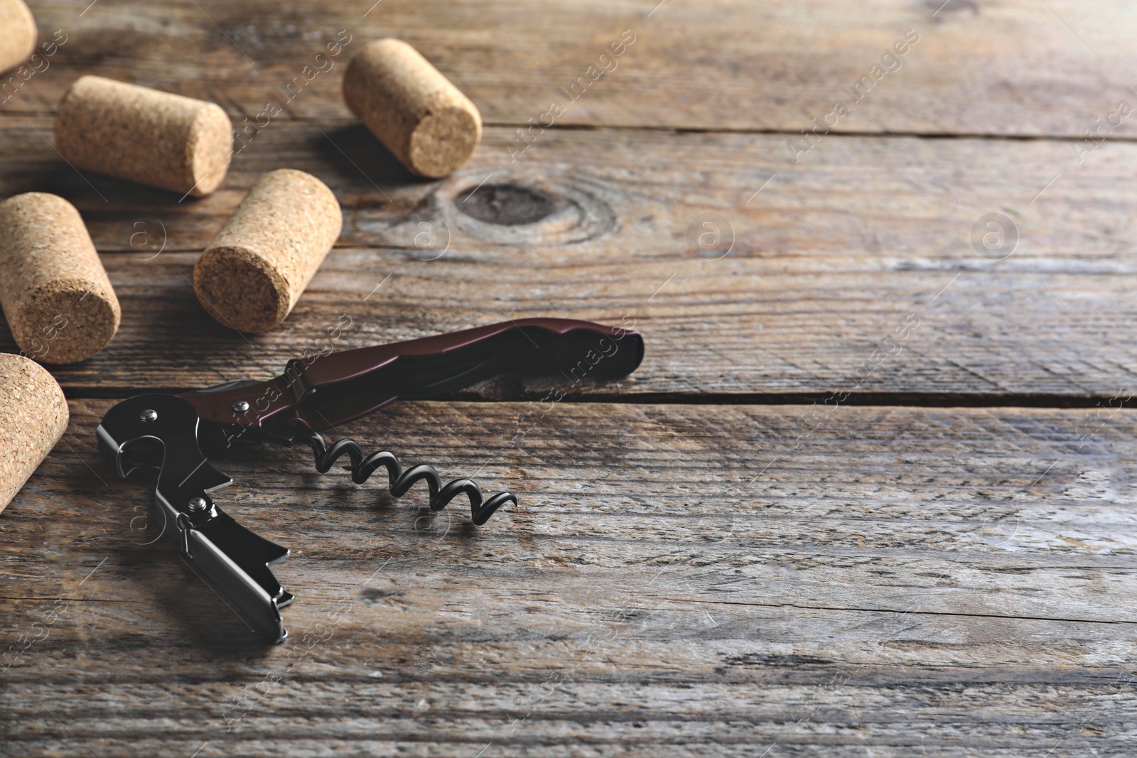 Image of Opener with corkscrew and corks on wooden table, space for text