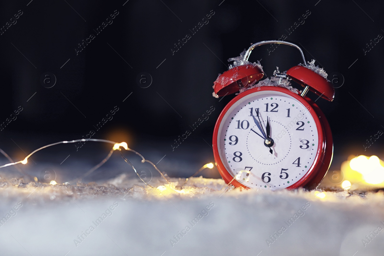 Photo of Alarm clock and Christmas lights on white snow outdoors, space for text. Midnight countdown