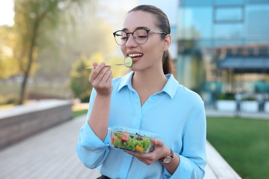 Photo of Portrait of smiling businesswoman eating from lunch box outdoors