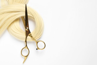 Photo of Professional hairdresser scissors with blonde hair strand on white background, top view
