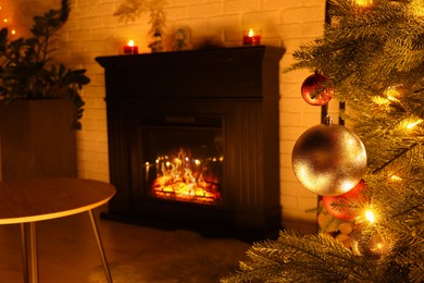 Christmas tree with baubles and festive lights near fireplace in room