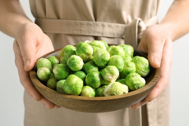 Photo of Woman holding wooden bowl with fresh Brussels sprouts, closeup