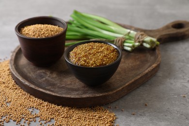 Serving board with delicious whole grain mustard, seeds and fresh green onion on grey table