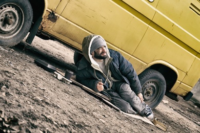 Poor homeless man lying near van outdoors