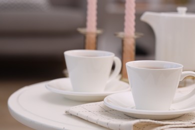 Cups of tea and teapot on white table indoors