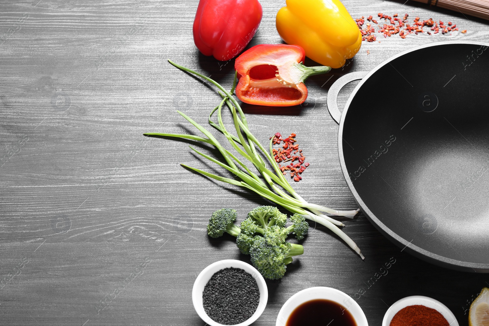 Photo of Empty iron wok and ingredients on dark grey wooden table. Space for text