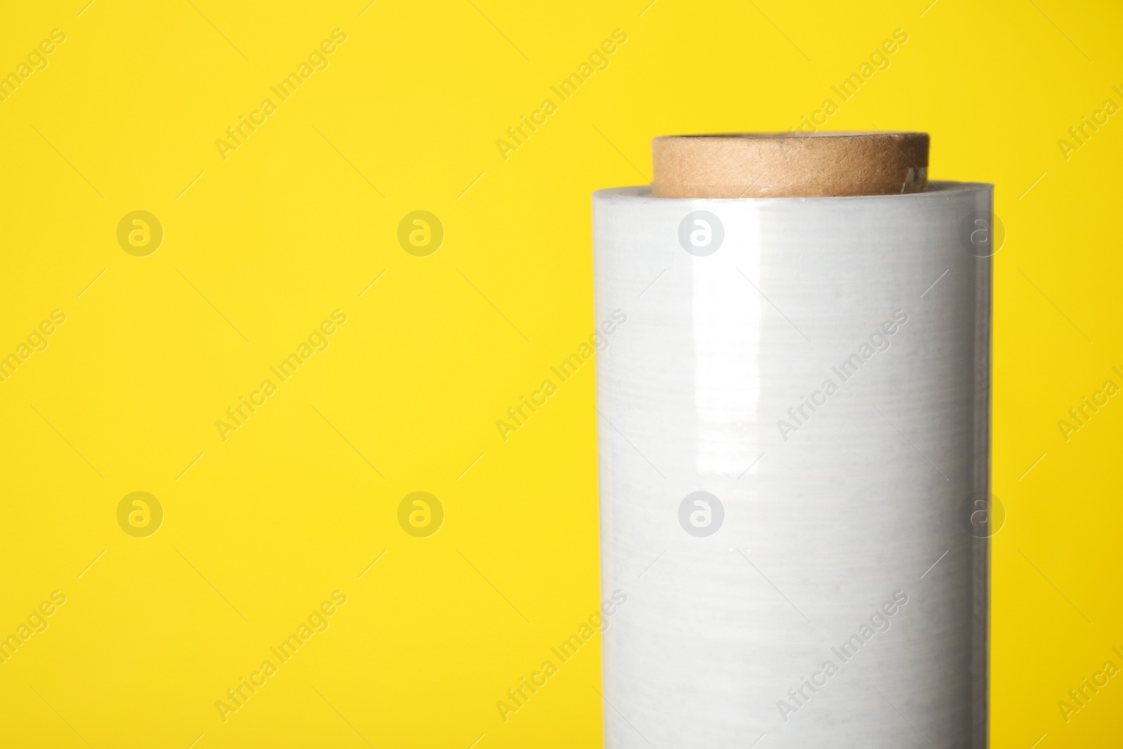 Photo of Roll of plastic stretch wrap film on yellow background, closeup. Space for text