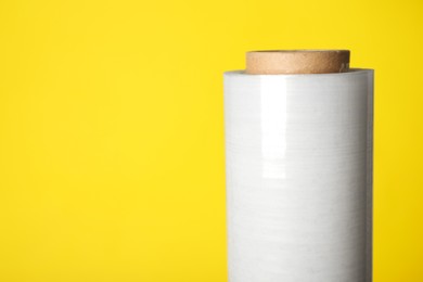 Photo of Roll of plastic stretch wrap film on yellow background, closeup. Space for text