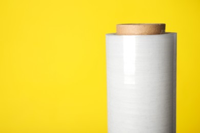 Roll of plastic stretch wrap film on yellow background, closeup. Space for text