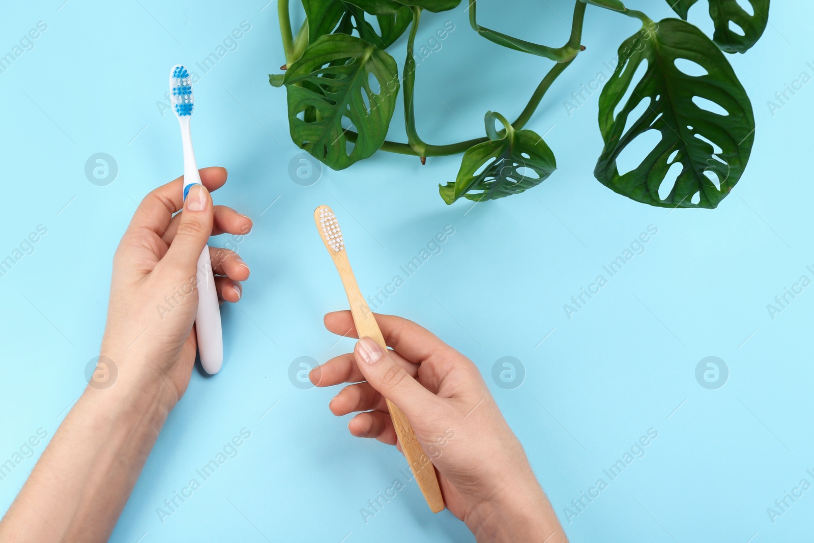 Photo of Woman holding natural bamboo and plastic toothbrushes on light blue background, above view