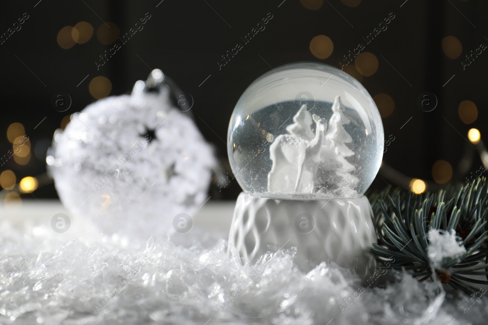 Photo of Christmas glass globe with artificial snow on table against blurred background