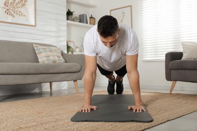 Handsome man doing plank exercise on yoga mat at home