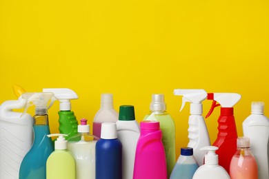 Many bottles of different detergents on yellow background, space for text. Cleaning supplies