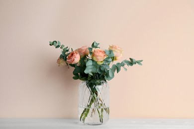 Photo of Vase with bouquet of beautiful roses on white wooden table near beige wall