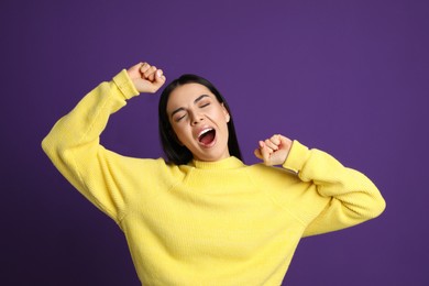 Young tired woman yawning on purple background