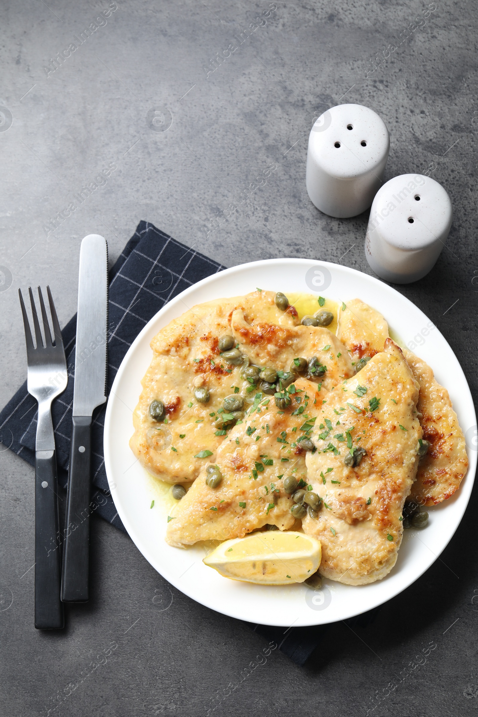 Photo of Delicious chicken piccata with herbs served on grey table, flat lay