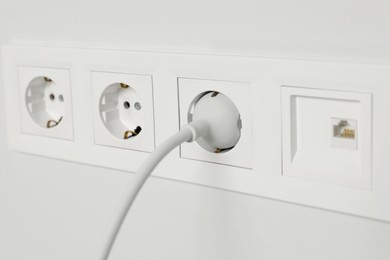 Photo of Power sockets with inserted plug on white wall, closeup. Electrical supply
