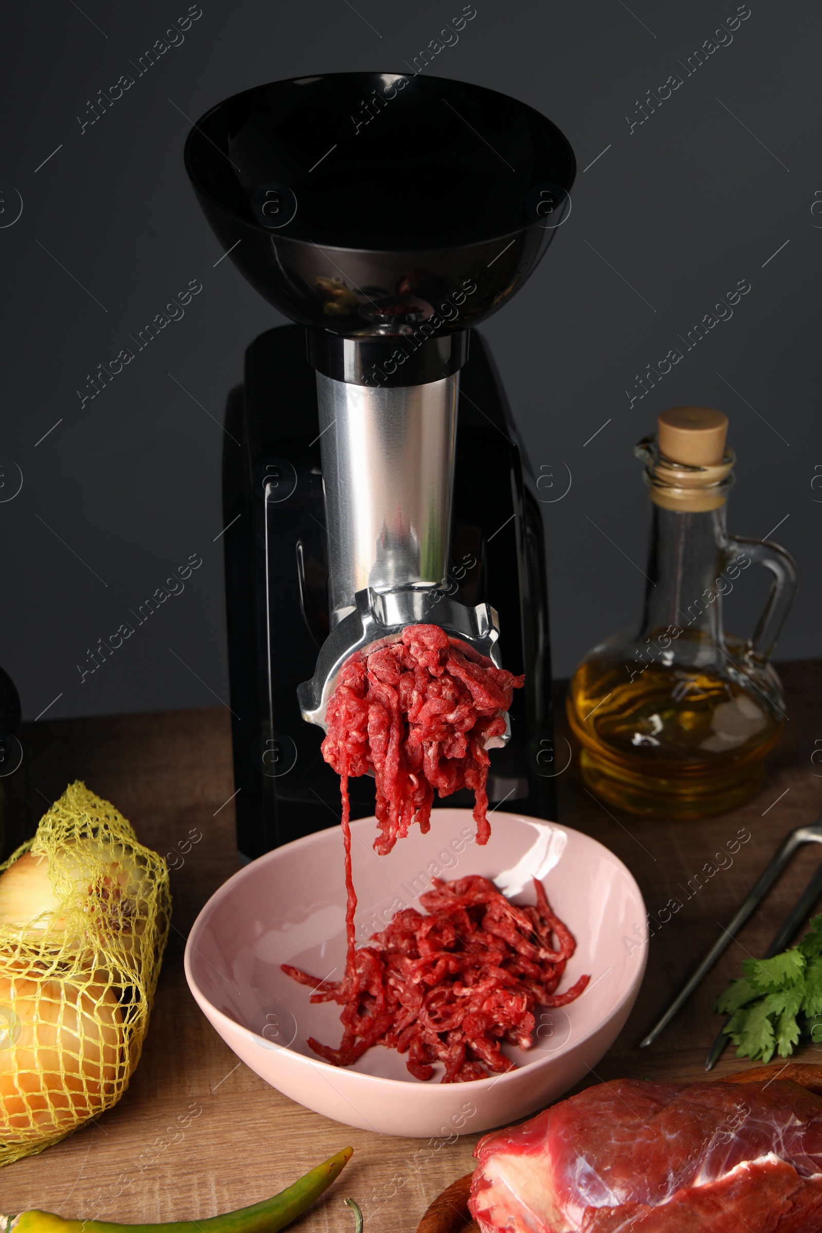 Photo of Electric meat grinder with minced beef and products on wooden table