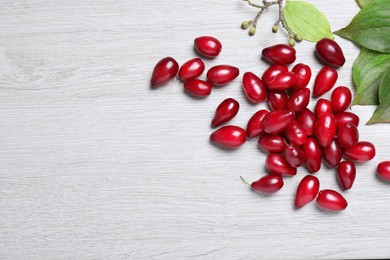 Photo of Pile of fresh ripe dogwood berries and green leaves on white wooden table, flat lay. Space for text