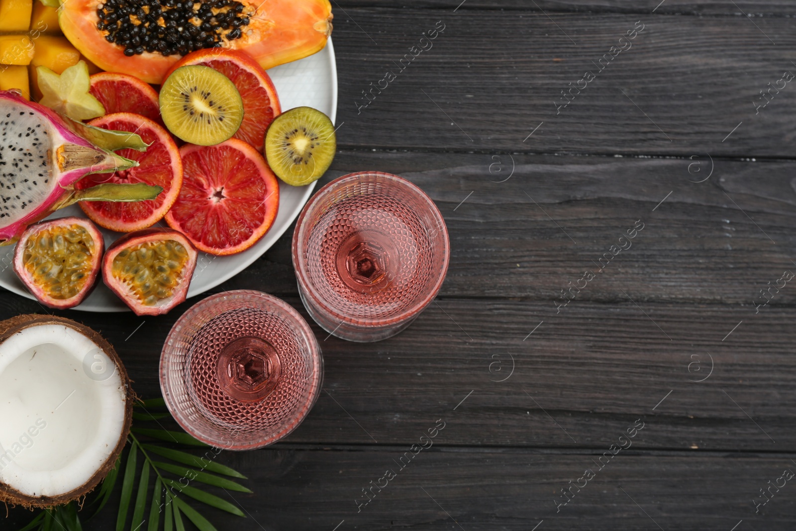 Photo of Delicious exotic fruits and wine on black wooden table, flat lay. Space for text