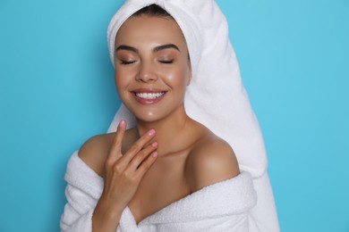 Photo of Beautiful young woman wearing bathrobe and towel on head against light blue background
