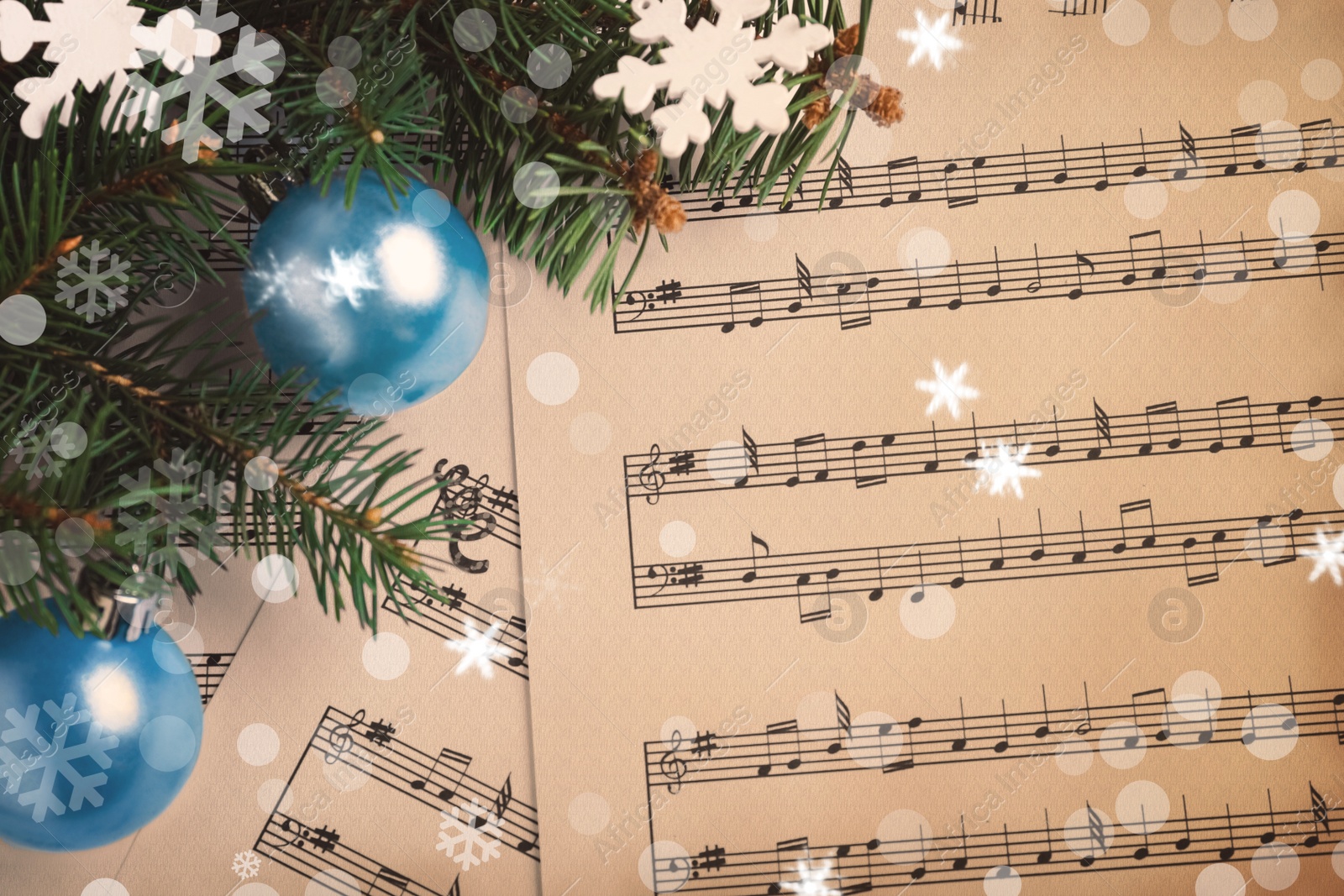 Image of Top view of fir tree branches with Christmas decor on sheet music pages, snowflakes and bokeh effect