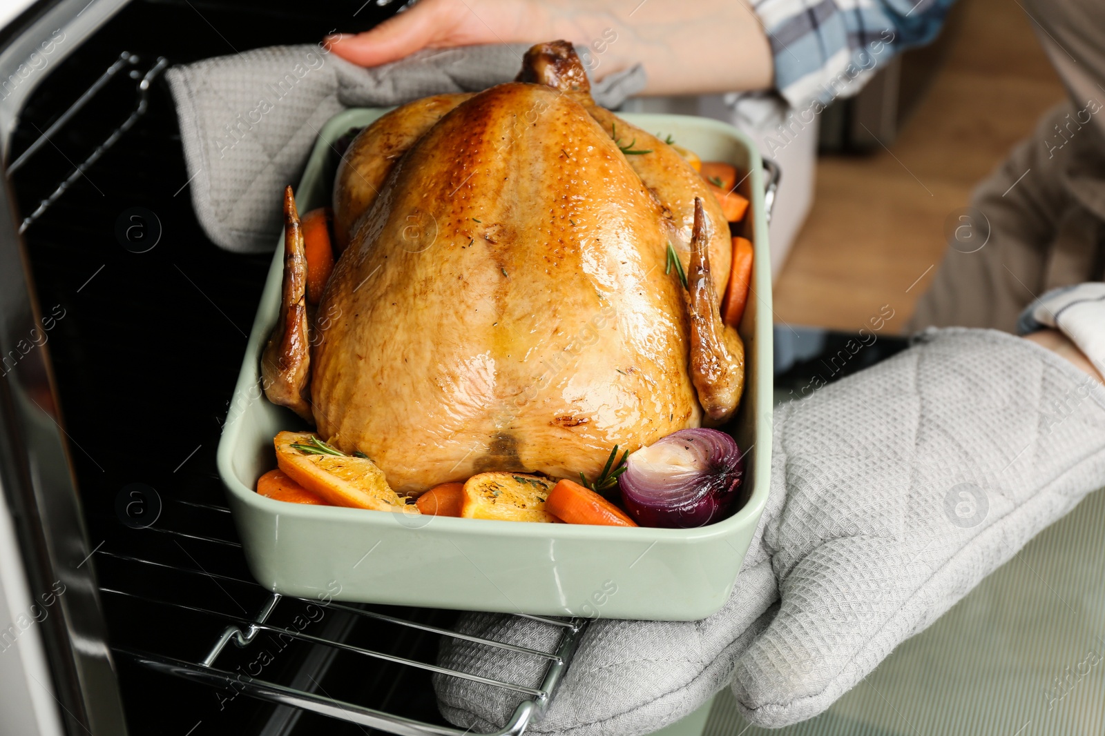 Photo of Woman taking baked chicken with oranges and vegetables out of oven, closeup