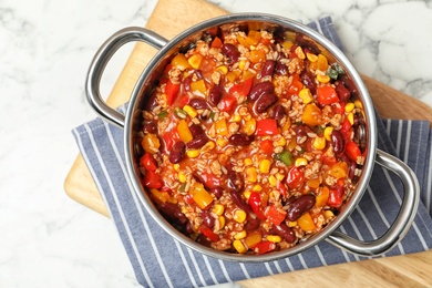 Wooden board with pan of chili con carne on marble table, top view