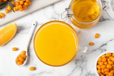 Photo of Fresh sea buckthorn tea on white marble table, flat lay